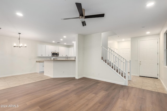 unfurnished living room with ceiling fan with notable chandelier, light hardwood / wood-style floors, and sink