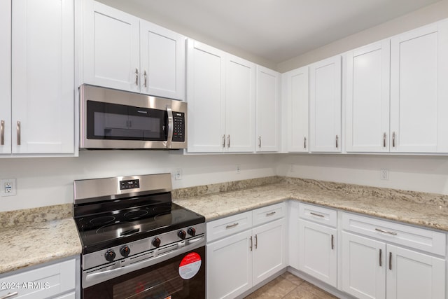 kitchen featuring white cabinets, light tile patterned floors, stainless steel appliances, and light stone counters