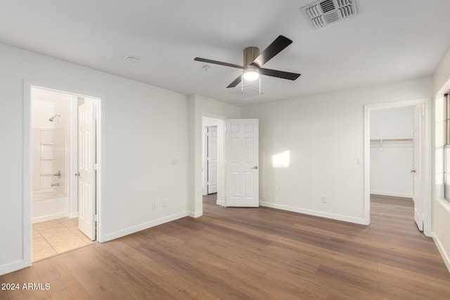 unfurnished bedroom featuring wood-type flooring, ensuite bathroom, a spacious closet, and ceiling fan