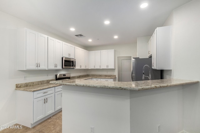 kitchen with kitchen peninsula, appliances with stainless steel finishes, light stone countertops, white cabinetry, and light tile patterned flooring