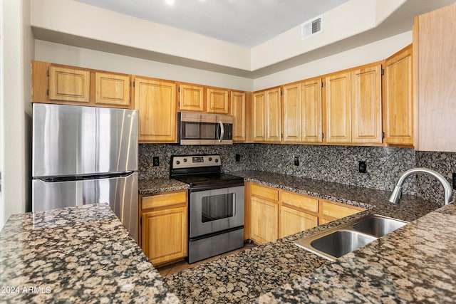 kitchen featuring dark stone counters, backsplash, appliances with stainless steel finishes, and sink