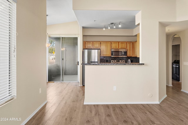 kitchen featuring tasteful backsplash, vaulted ceiling, light hardwood / wood-style flooring, appliances with stainless steel finishes, and dark stone countertops