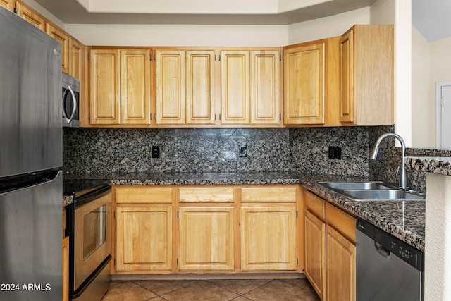 kitchen featuring appliances with stainless steel finishes, dark stone countertops, tasteful backsplash, light tile patterned floors, and sink