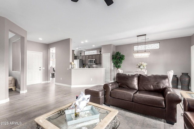 living room featuring ceiling fan with notable chandelier, a wealth of natural light, and light hardwood / wood-style floors