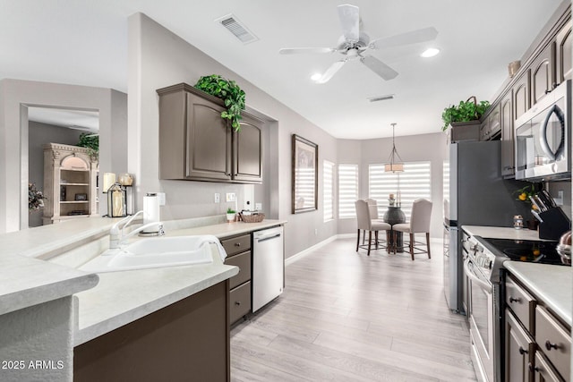 kitchen with sink, light hardwood / wood-style flooring, ceiling fan, appliances with stainless steel finishes, and decorative light fixtures