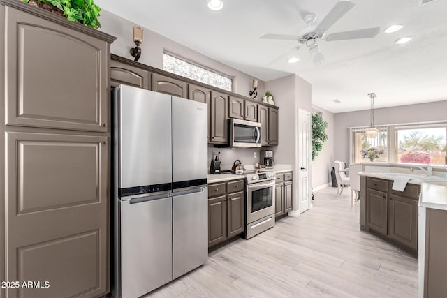 kitchen featuring sink, light wood-type flooring, pendant lighting, ceiling fan, and stainless steel appliances