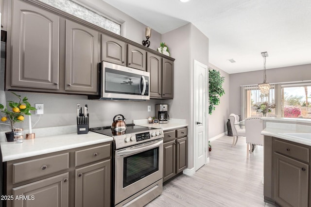 kitchen featuring stainless steel appliances, light wood-type flooring, and decorative light fixtures