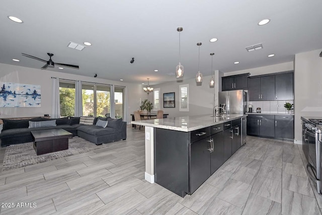 kitchen featuring stainless steel refrigerator with ice dispenser, sink, decorative light fixtures, gas stove, and an island with sink