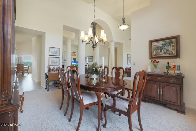 carpeted dining area featuring a chandelier, decorative columns, and high vaulted ceiling