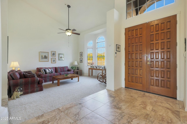 foyer entrance with ceiling fan, light colored carpet, and a towering ceiling