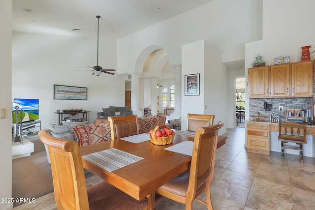 dining space with ceiling fan, ornate columns, and a towering ceiling