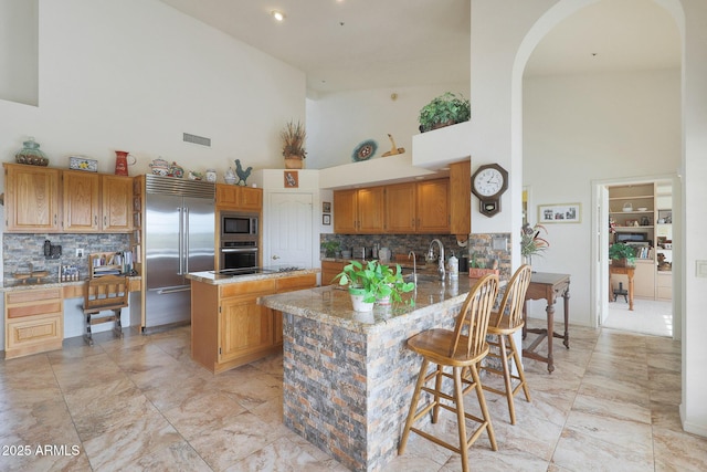 kitchen featuring backsplash, built in appliances, high vaulted ceiling, and a kitchen island