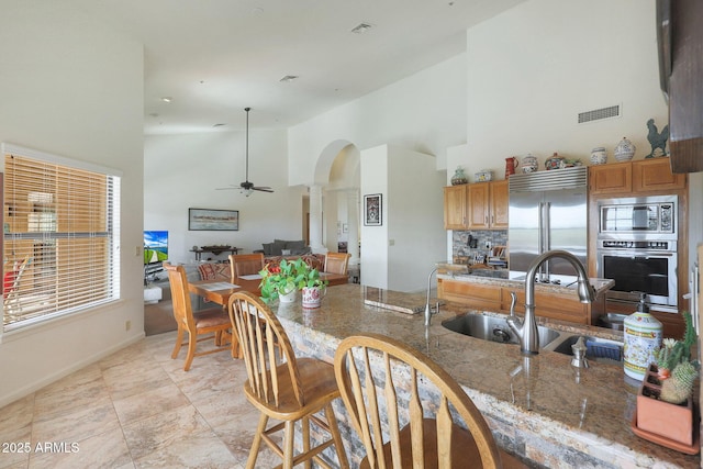 kitchen with stone counters, high vaulted ceiling, sink, built in appliances, and ceiling fan