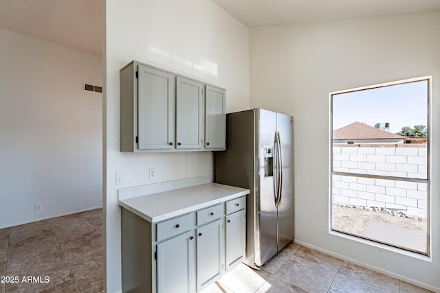 kitchen with gray cabinetry, a towering ceiling, and stainless steel refrigerator with ice dispenser