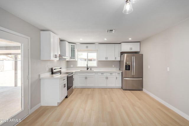 kitchen with sink, light hardwood / wood-style floors, white cabinets, exhaust hood, and appliances with stainless steel finishes