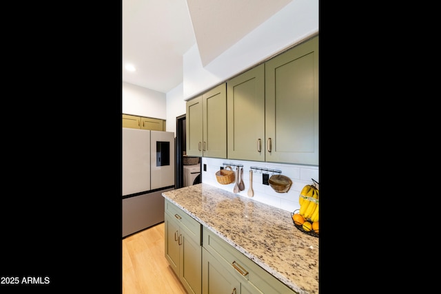 kitchen featuring light wood-style flooring, light stone counters, freestanding refrigerator, separate washer and dryer, and decorative backsplash