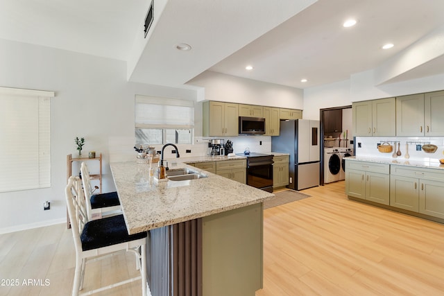 kitchen featuring stainless steel microwave, washer / dryer, freestanding refrigerator, black / electric stove, and a sink