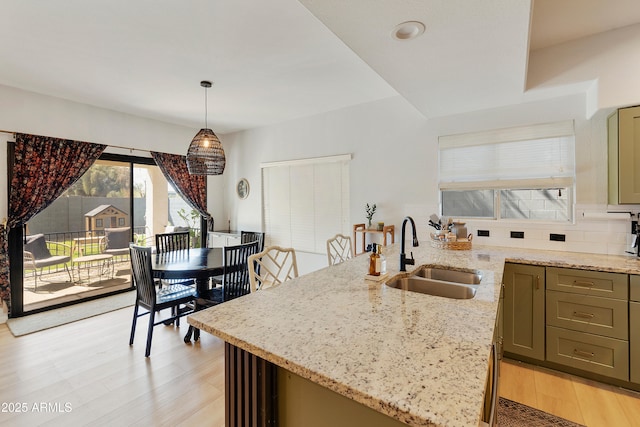 kitchen featuring light stone countertops, a peninsula, light wood-style flooring, a sink, and pendant lighting