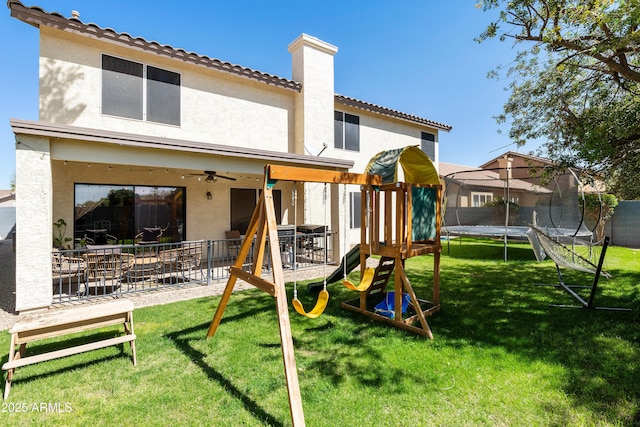 view of play area featuring a lawn, a ceiling fan, a trampoline, and fence