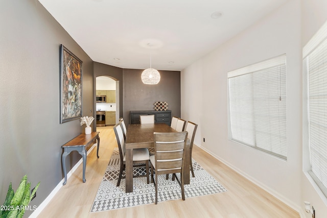 dining room featuring baseboards, arched walkways, and light wood finished floors