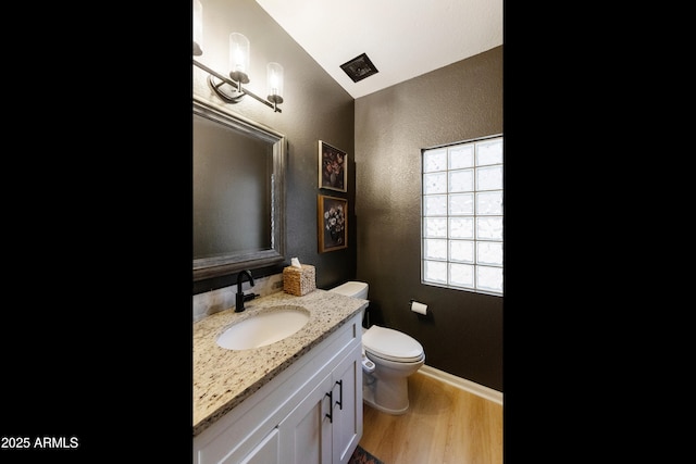 bathroom featuring vanity, wood finished floors, baseboards, toilet, and a textured wall