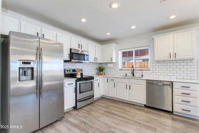 kitchen featuring appliances with stainless steel finishes, a sink, light countertops, white cabinetry, and recessed lighting