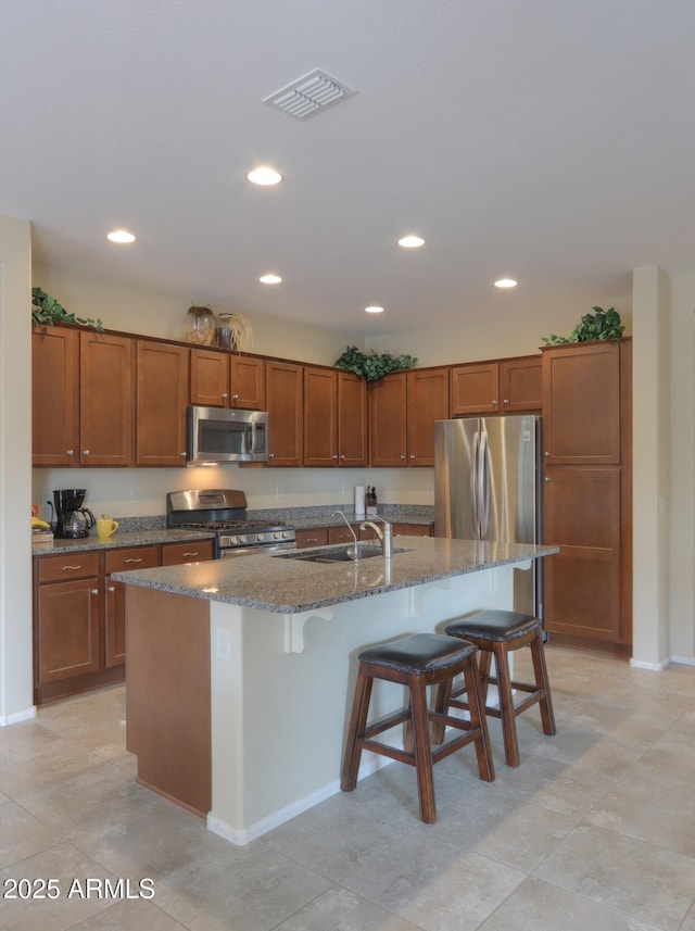 kitchen featuring appliances with stainless steel finishes, a breakfast bar, sink, dark stone counters, and a center island with sink