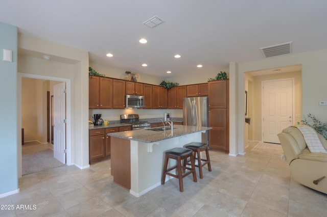 kitchen with an island with sink, sink, dark stone countertops, a kitchen breakfast bar, and stainless steel appliances