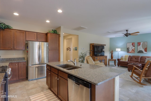 kitchen with sink, ceiling fan, appliances with stainless steel finishes, light stone countertops, and a center island with sink