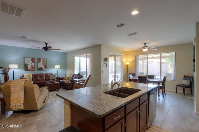 kitchen with dishwasher, sink, a kitchen island with sink, light tile patterned floors, and light stone counters