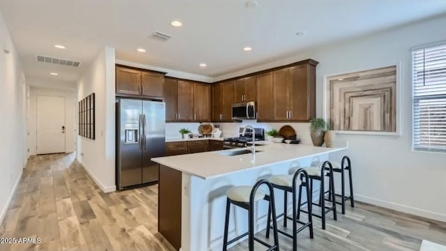 23334 W Mobile Ln, Buckeye, AZ 85326 - kitchen featuring stainless steel appliances, a sink, a peninsula, light wood finished floors, and a breakfast bar