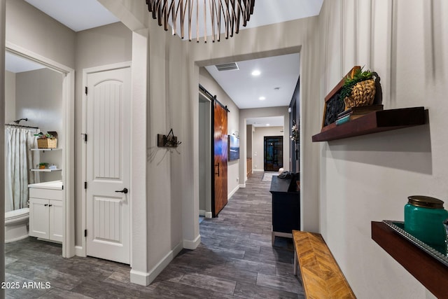 hallway featuring dark wood-style floors, baseboards, visible vents, recessed lighting, and a barn door