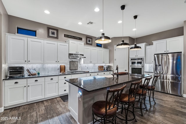 kitchen featuring visible vents, under cabinet range hood, dark wood-style floors, appliances with stainless steel finishes, and decorative backsplash