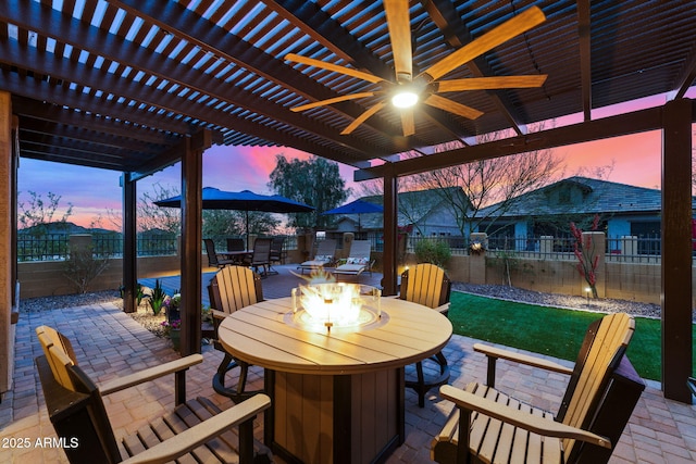 patio terrace at dusk featuring a ceiling fan, outdoor dining area, a fenced backyard, a pergola, and a fire pit