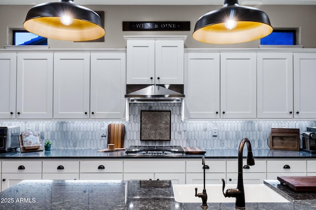 kitchen with ventilation hood, a sink, decorative backsplash, stainless steel gas stovetop, and white cabinetry