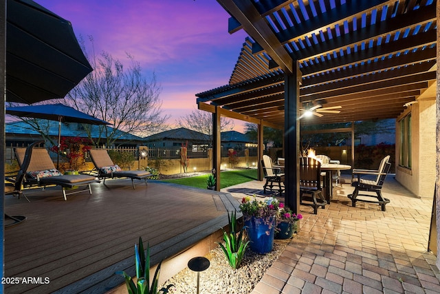 patio terrace at dusk with outdoor dining area, a pergola, and a wooden deck