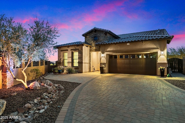 mediterranean / spanish-style house featuring decorative driveway, stucco siding, an attached garage, and fence