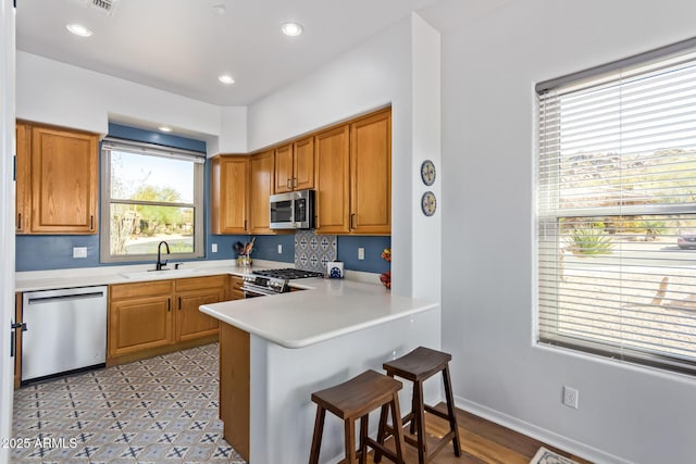 kitchen with a peninsula, a sink, light countertops, appliances with stainless steel finishes, and a kitchen bar