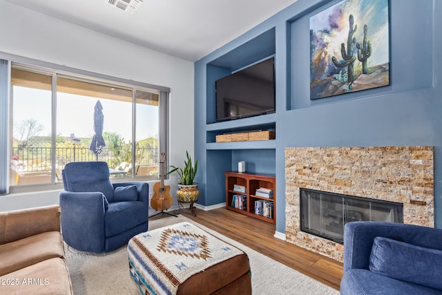 living room featuring a stone fireplace, wood finished floors, visible vents, and baseboards