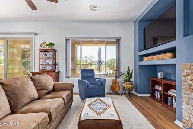 living area featuring a ceiling fan, wood finished floors, visible vents, and baseboards