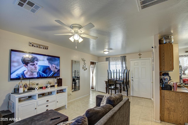 living area featuring light tile patterned floors, visible vents, a textured ceiling, and a ceiling fan