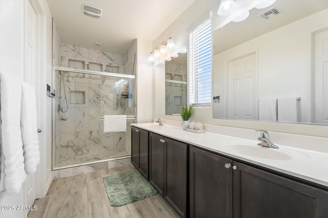 bathroom featuring a sink, visible vents, a marble finish shower, and wood finished floors