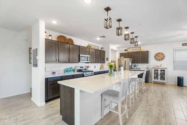 kitchen with light wood finished floors, dark brown cabinets, appliances with stainless steel finishes, and light countertops