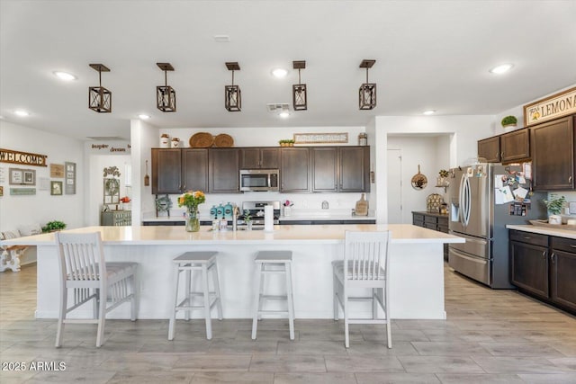 kitchen featuring a kitchen bar, a spacious island, stainless steel appliances, light countertops, and dark brown cabinets