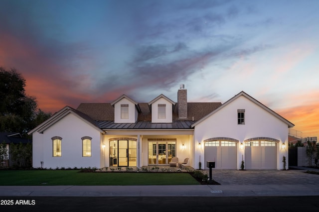 view of front of house featuring a standing seam roof, stucco siding, decorative driveway, and a front yard