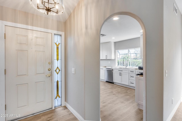 foyer entrance featuring arched walkways, visible vents, light wood-style floors, a chandelier, and baseboards