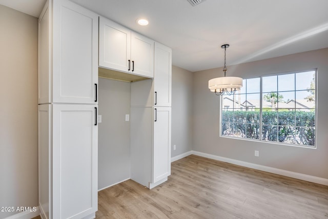 unfurnished dining area with baseboards, a chandelier, and light wood-style floors