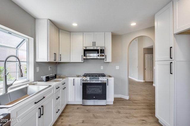 kitchen featuring arched walkways, stainless steel appliances, a sink, white cabinets, and light wood-type flooring