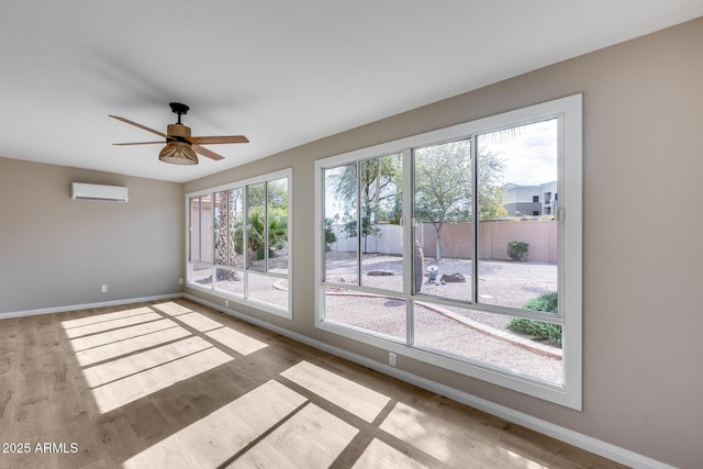 empty room with a ceiling fan, a wall unit AC, baseboards, and wood finished floors