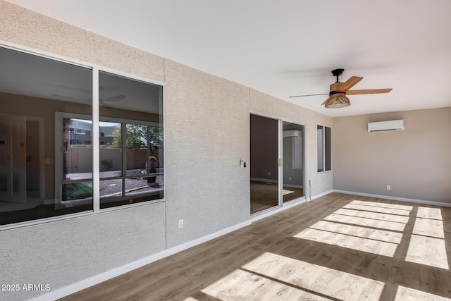 empty room featuring ceiling fan, baseboards, wood finished floors, and a wall mounted air conditioner